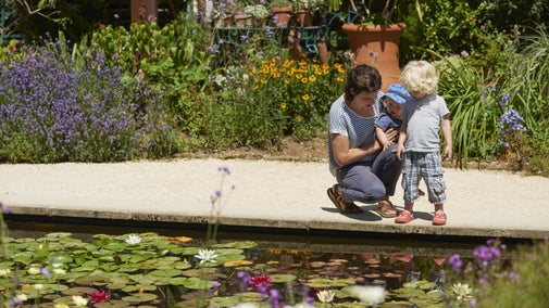 Mother and children kneeling by a lily pond at Hidcote, Gloucestershire
